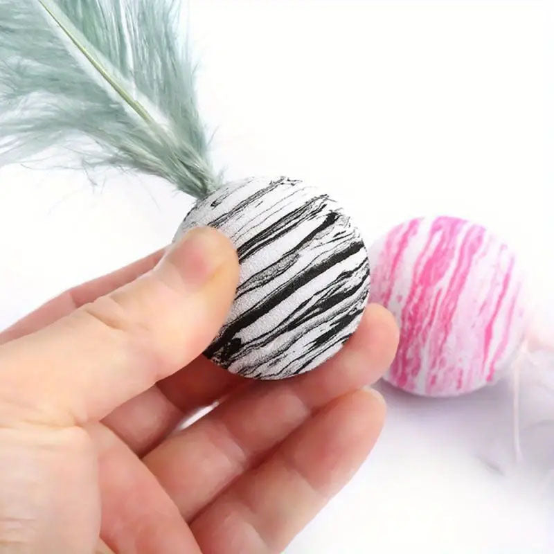 hand holding a cat ball toy with feathers